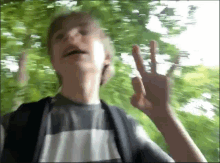 a young boy is giving a peace sign in front of some trees