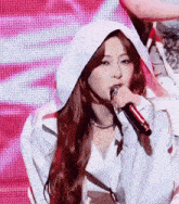 a woman is singing into a microphone while wearing a white hooded jacket .
