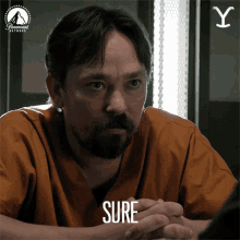 a man with a beard is wearing an orange scrub top and the word sure is on his face