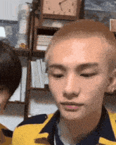 a man with a shaved head is standing next to another man in a room with a clock in the background .
