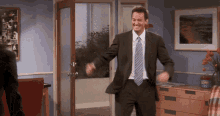 a man in a suit and tie is dancing in a room with a jar of knorr on the dresser