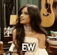 a woman in a white dress is standing in front of a guitar and saying ew .