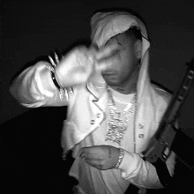 a black and white photo of a man holding a gun and wearing a white hoodie
