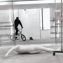 a mannequin is laying on the floor in front of a man riding a bike