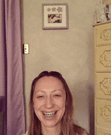 a woman with braces on her teeth smiles in front of a picture on the wall
