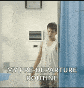 a man in a white tank top is standing in a room with a blue curtain .