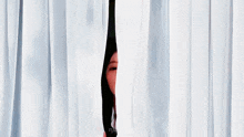 a woman is peeking out from behind a white curtain and making a funny face .