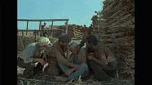 a group of men are gathered around a man sitting in the dirt