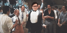 a man in a tuxedo is dancing with a group of men in suits and ties .