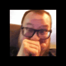 a man with glasses and a beard is coughing into his hand .