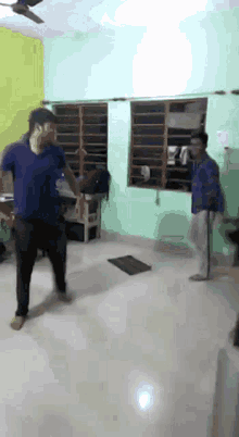 a man in a blue shirt is dancing in a room with a ceiling fan
