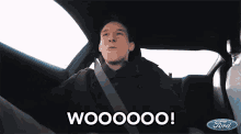 a man sitting in a car with the words wooooo on the screen