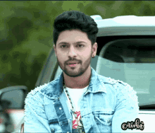a man wearing a denim jacket with pearls on the sleeves is standing in front of a car