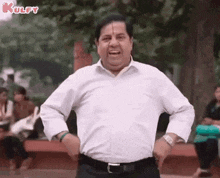 a man in a white shirt is standing in a park with his hands on his hips .