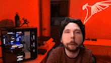 a man with a beard is sitting in front of a computer in a room with a red wall .