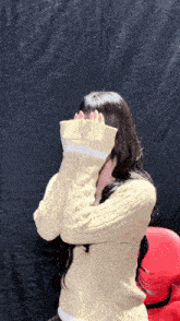 a woman in a tan sweater covering her face with her arms