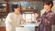 a man in a plaid shirt is standing next to a man in a white sweater in a kitchen