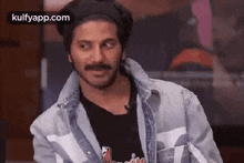 a man with a mustache wearing a denim jacket and a black shirt is making a funny face .