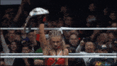 a woman in a wrestling ring holds up her championship belt in front of a crowd