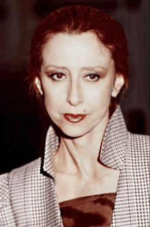 a woman with red hair is wearing a plaid jacket and earrings