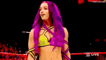 a woman with purple hair and a yellow top is standing in a ring .