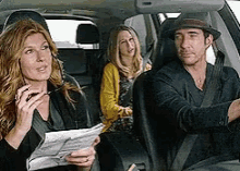 a man in a hat is driving a car with two women in the back seat .