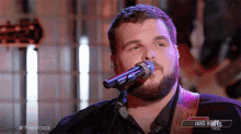 a man with a beard singing into a microphone on nbc 's the voice