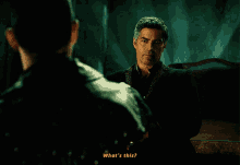 a man in a black jacket shakes hands with another man in a dark room and says " what 's this "