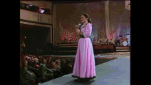 a woman in a pink dress singing into a microphone on stage