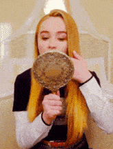 a woman looks at herself in a hand mirror while sitting on a bed