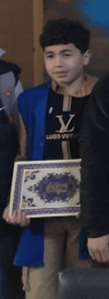 a young boy wearing a louis vuitton shirt holds a framed certificate