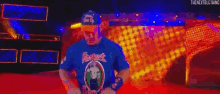 a man in a blue shirt and hat is standing on a stage in front of a colorful background .