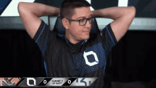 a man wearing glasses sits in a chair with his hands behind his head and a game 1 up next banner behind him