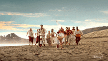 a group of people running on a beach with a disney logo on the bottom right