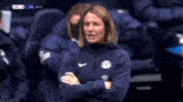 a woman wearing a nike jacket stands with her arms crossed during a soccer match