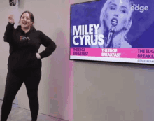 a woman is standing in front of a screen that says miley cyrus