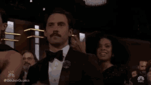 a man in a tuxedo with a mustache is applauding while sitting in a crowd .