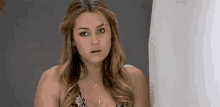 a woman in a bikini is standing in front of a shower curtain making a surprised face .