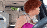 a woman with red hair is sitting in a car wearing a necklace
