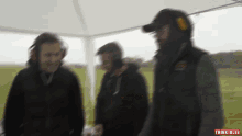 three men are standing under a white tent and the words think jules are on the bottom right