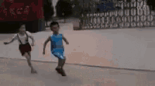 a boy in a blue shirt is running with a girl in red shorts behind him