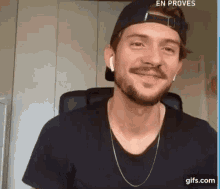 a man with a beard wearing a hat and ear buds is smiling while sitting in a chair .