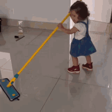 a little girl is holding a mop with a yellow handle