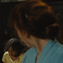 a woman in a yellow shirt is looking at another woman in a blue dress