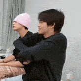 a man wearing a pink hat is sitting next to another man .