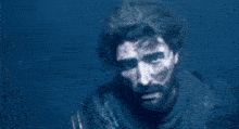a man with a beard and blood on his face is standing in a dark room .