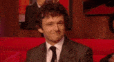 a man in a suit and tie is smiling and clapping his hands .
