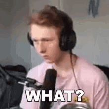 a young man wearing headphones and a pink shirt is sitting in front of a microphone and making a funny face .
