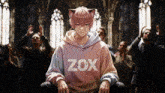 a boy wearing a hoodie that says zox sits in front of a crowd of people