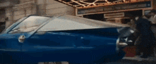 a blue car is parked in front of a building and a man is standing next to it .